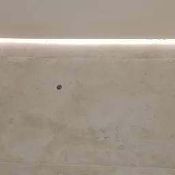 Wykończona ściana w łazience z szarych płytek imitujących beton, oświetlenie LED w suficie i białe kwadratowe płytki na ścianach bocznych.