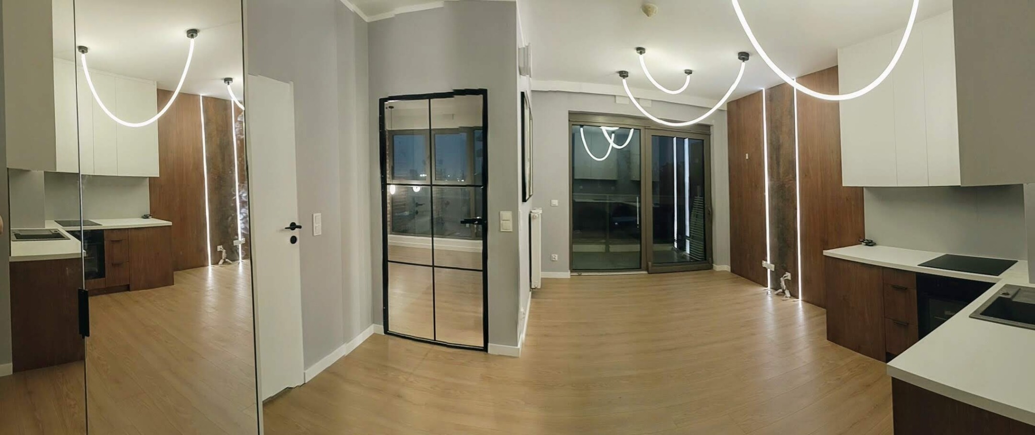 Nowoczesne wnętrze: parkiet, zabudowa kuchenna z oświetleniem LED, przeszklone drzwi w czarnej ramie. Minimalistyczny design mieszkania po remoncie.
