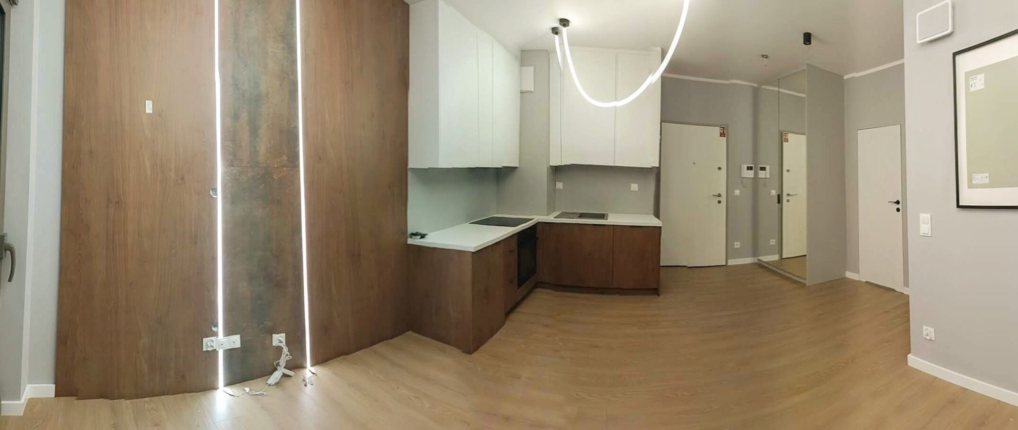 Nowoczesne wykończenie wnętrza kuchni z drewnianymi panelami ściennymi i oświetleniem LED. Widok na minimalistyczne szafki i blaty, aranżacja w odcieniach bieli i brązu.