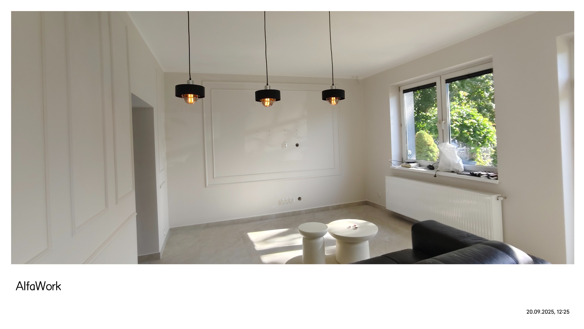 Jasne wnętrze po remoncie: białe ściany z dekoracyjnymi listwami, trzy lampy wiszące, okno z widokiem na zieleń, nowoczesne meble. Minimalistyczny design z dbałością o detale.