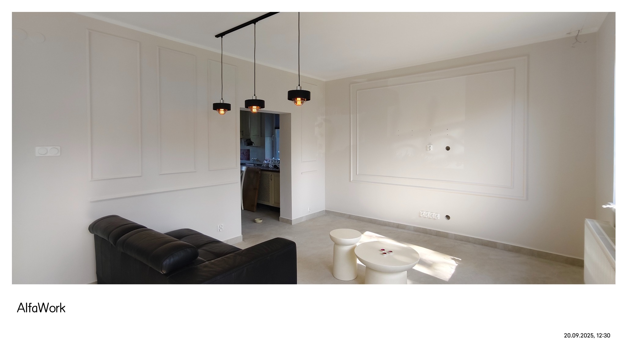 Kremowe ściany z dekoracyjnymi panelami i listwami w salonie. Nowoczesne oświetlenie i meble. Widok na kuchnię w tle. Minimalistyczny wystrój wnętrza.