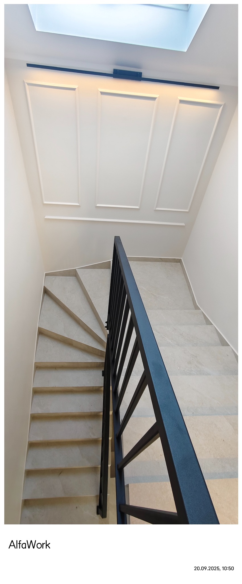 Wykończone schody spiralne z beżową okładziną i czarną metalową balustradą. Białe ściany z dekoracyjnymi panelami i oświetleniem LED pod sufitem.