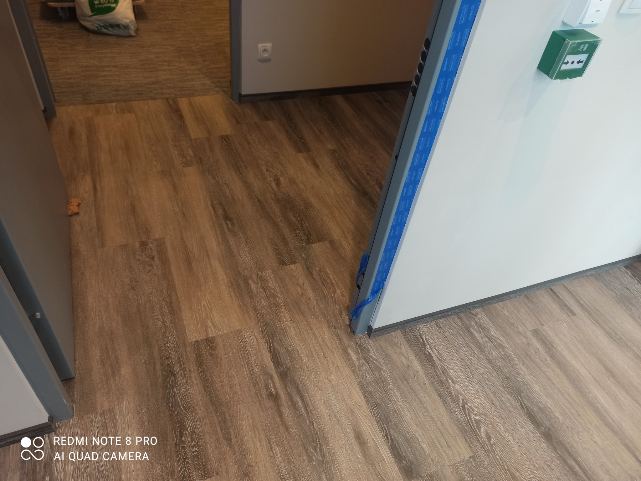 Nowo ułożone panele podłogowe z wzorem drewna, widoczne zabezpieczenia na ościeżnicy drzwi.