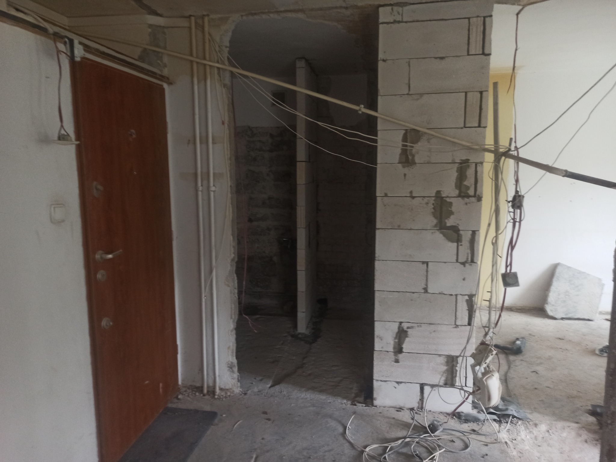 Wnętrze w trakcie remontu: widoczne ściany z betonu komórkowego, wystające przewody elektryczne, stara futryna drzwiowa i fragmenty gruzu na podłodze.