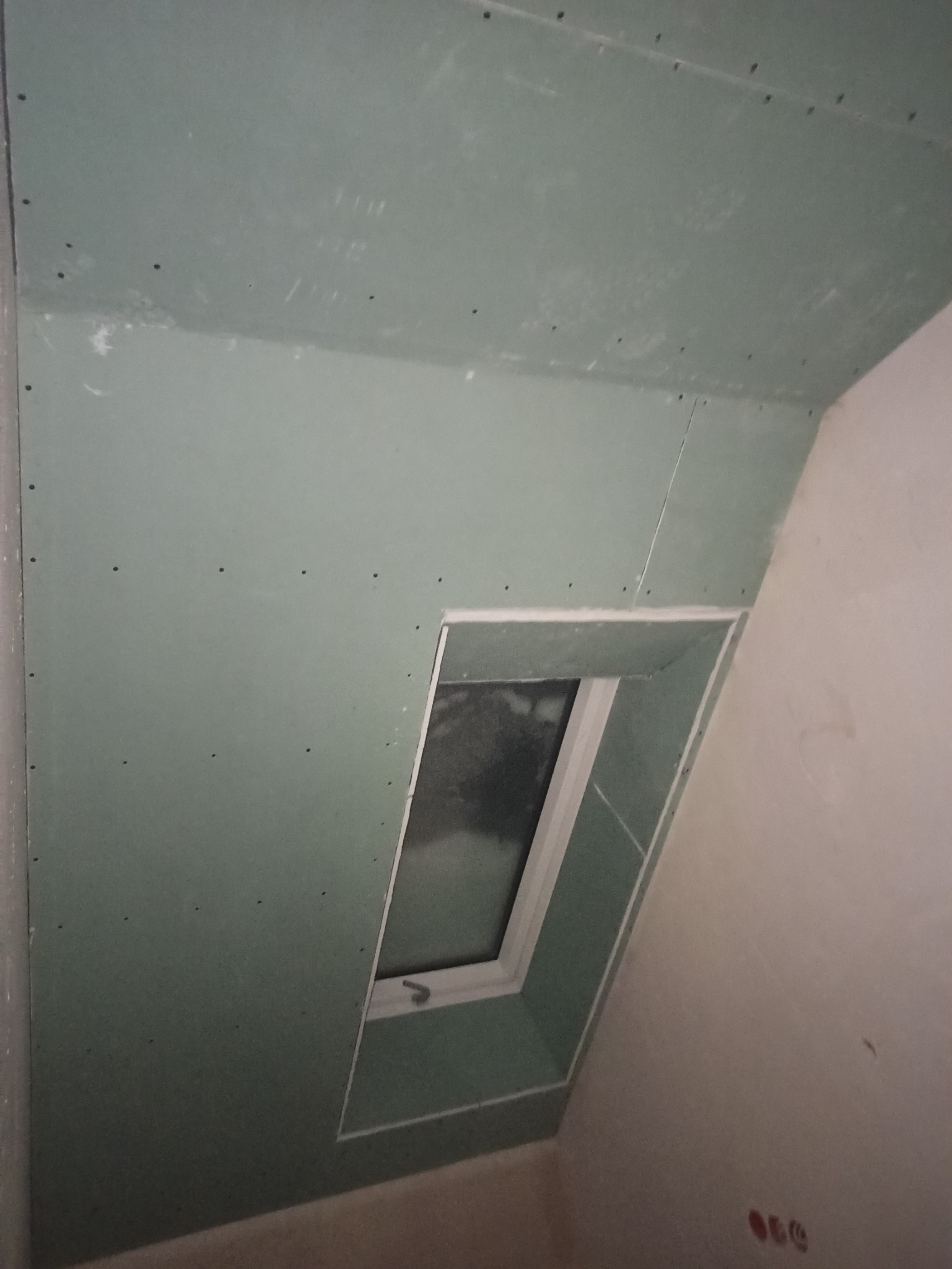 Montaż płyt kartonowo-gipsowych wokół okna dachowego na poddaszu, widoczne ślady po wkrętach.