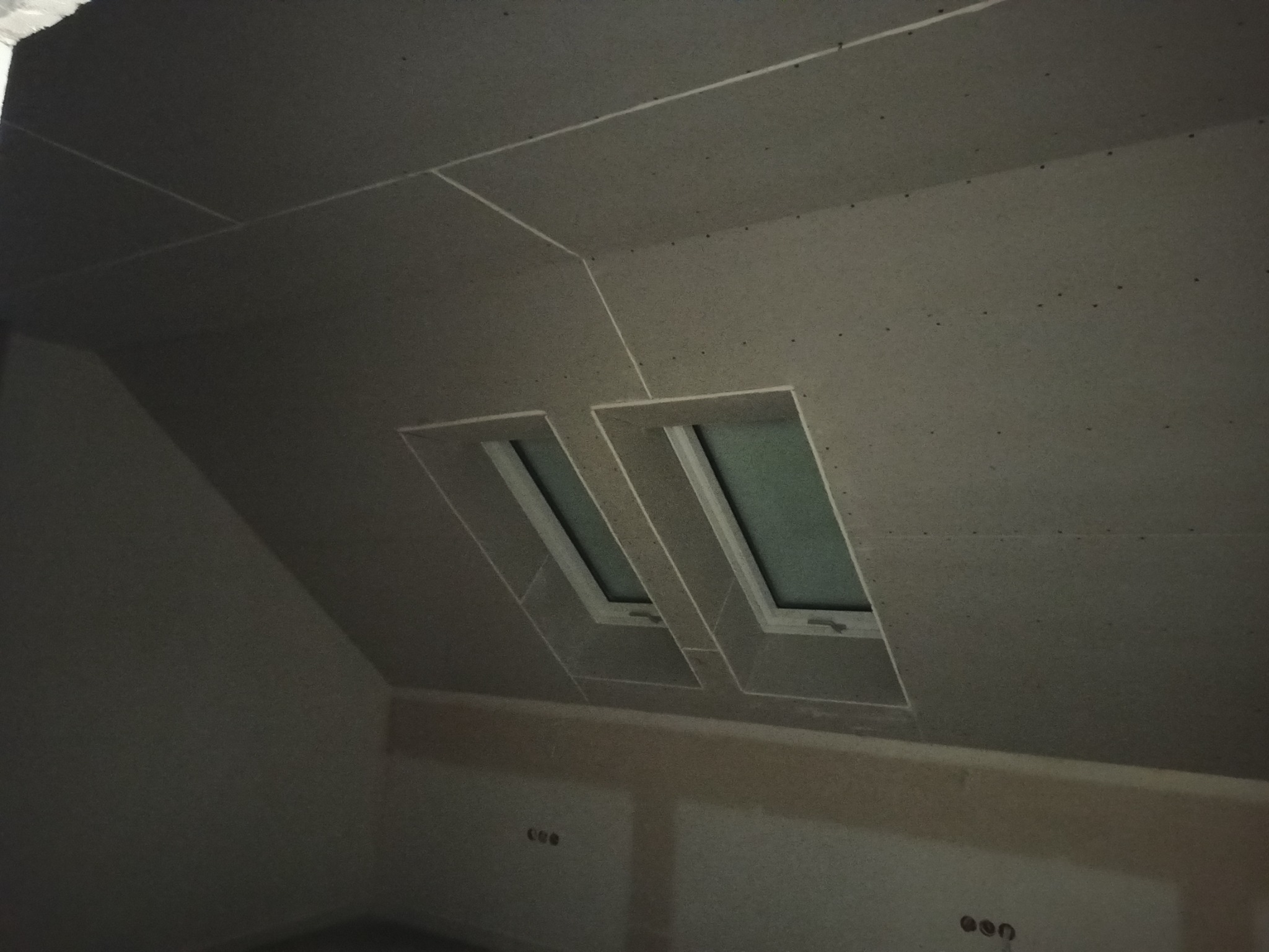 Poddasze z dwoma oknami dachowymi, wykończone płytami kartonowo-gipsowymi, widoczne szpachlowane łączenia płyt i otwory po wkrętach.