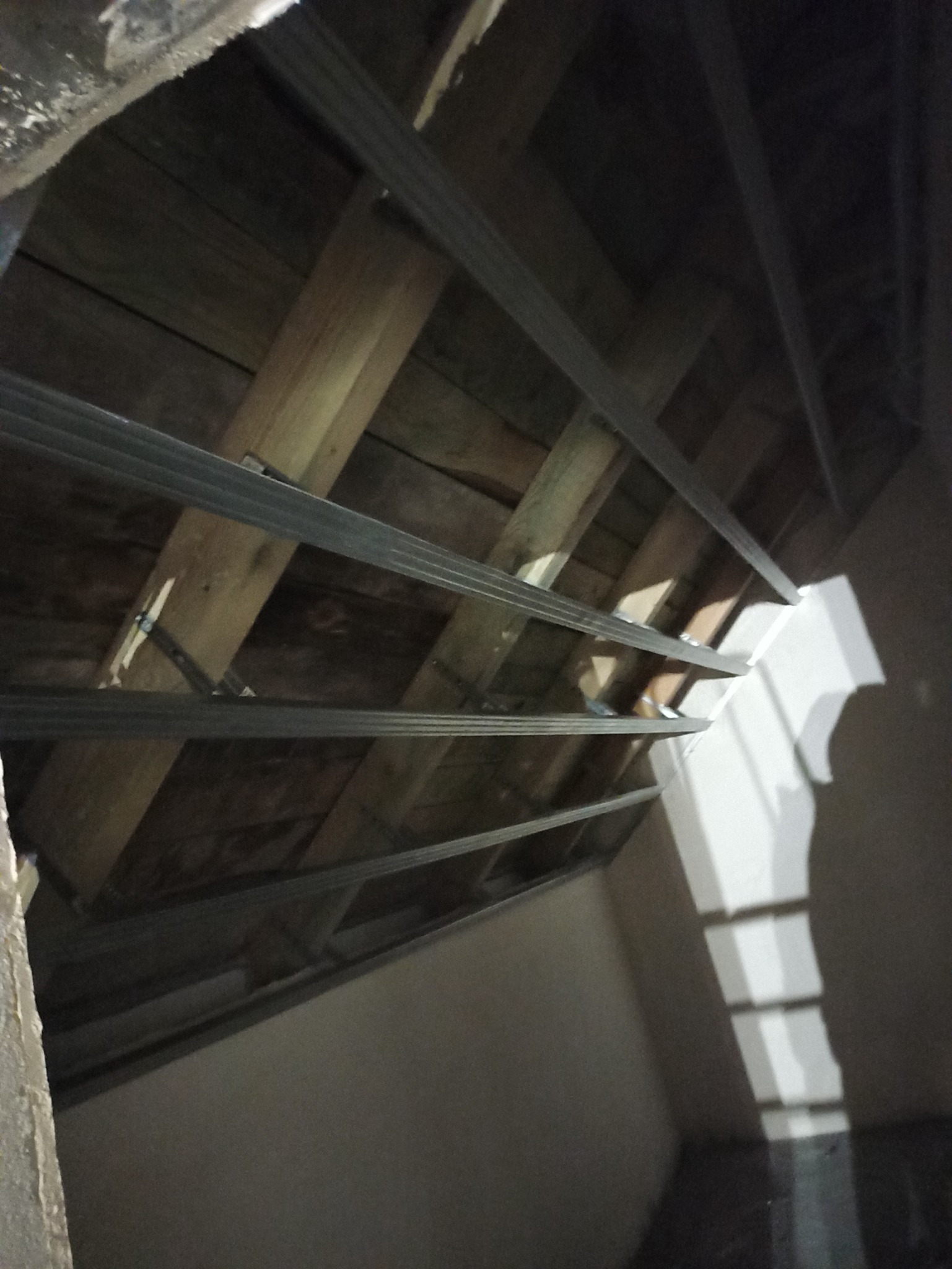 Montaż metalowej konstrukcji sufitu podwieszanego z płyt karton gips na drewnianej więźbie dachowej, widoczne profile i elementy mocujące.