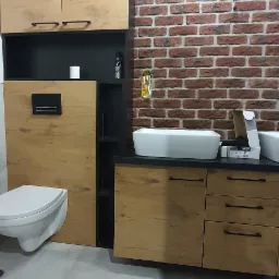 Nowoczesna łazienka z wiszącą toaletą i szafkami z drewnianym fornirem, umywalka nablatowa i ściana z czerwonej cegły.