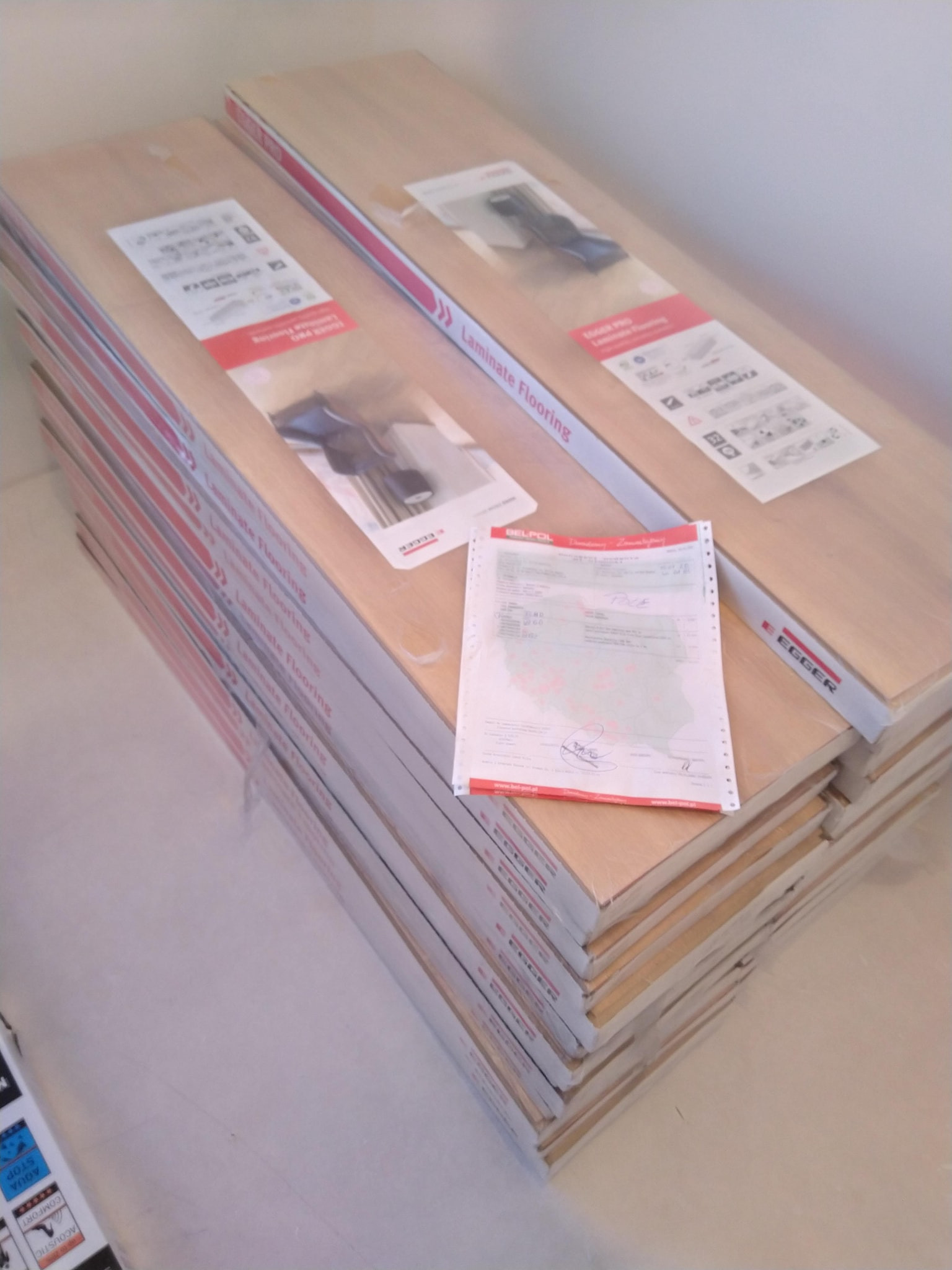 Stosy zapakowanych paneli podłogowych laminowanych marki Egger, na wierzchu faktura od Belpol