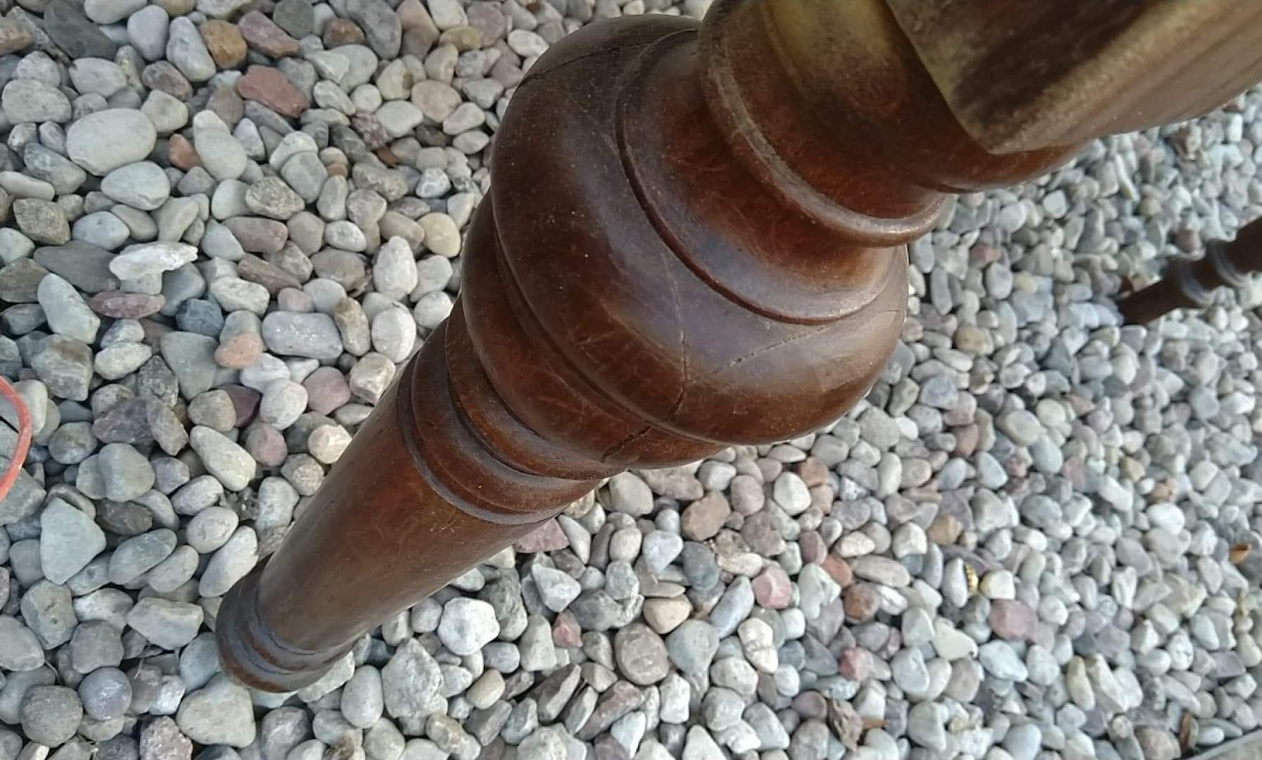 Fragment toczonej nogi drewnianego mebla z widocznymi śladami użytkowania, umieszczonej na tle drobnych, szarych kamieni.