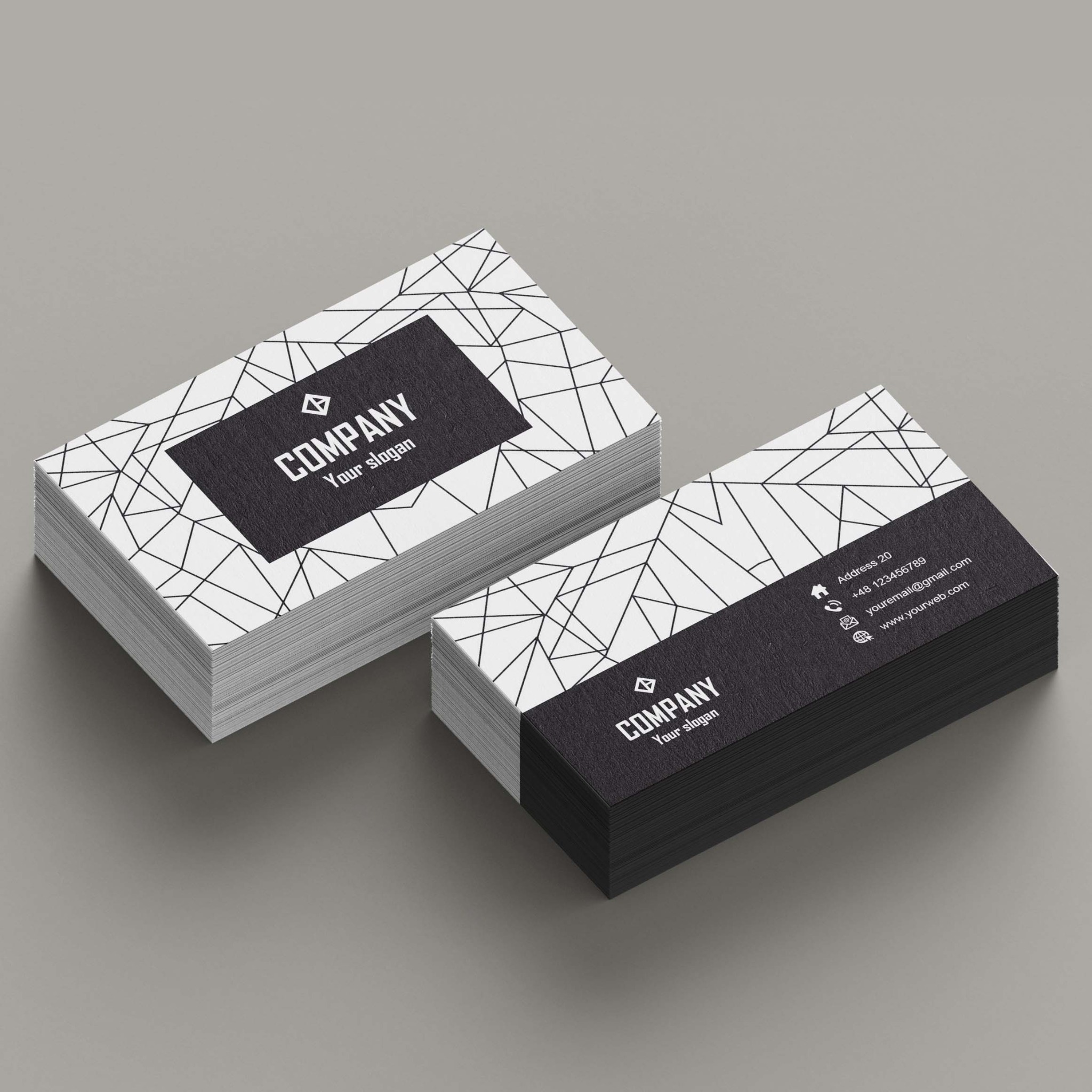 Dwa stosy wizytówek z czarnym tłem i białym geometrycznym wzorem, leżące na szarym tle. Wizytówki zawierają logo firmy i dane kontaktowe.