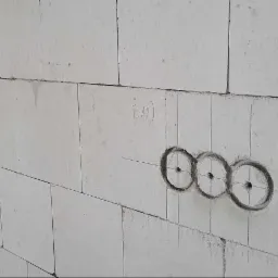 Ściana z betonu komórkowego z zaznaczonymi otworami pod puszki elektryczne, widoczne linie pomocnicze i oznaczenia ołówkiem.