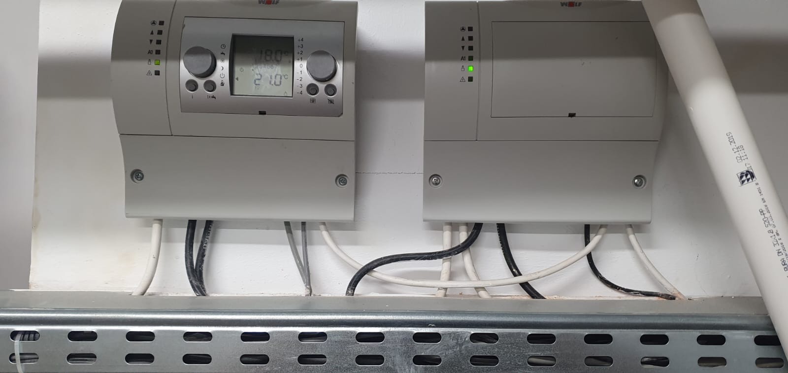 Dwa panele sterowania Wolf zamontowane na ścianie, z widocznymi przewodami elektrycznymi i rurą PCV z datą produkcji 02.12.2019.