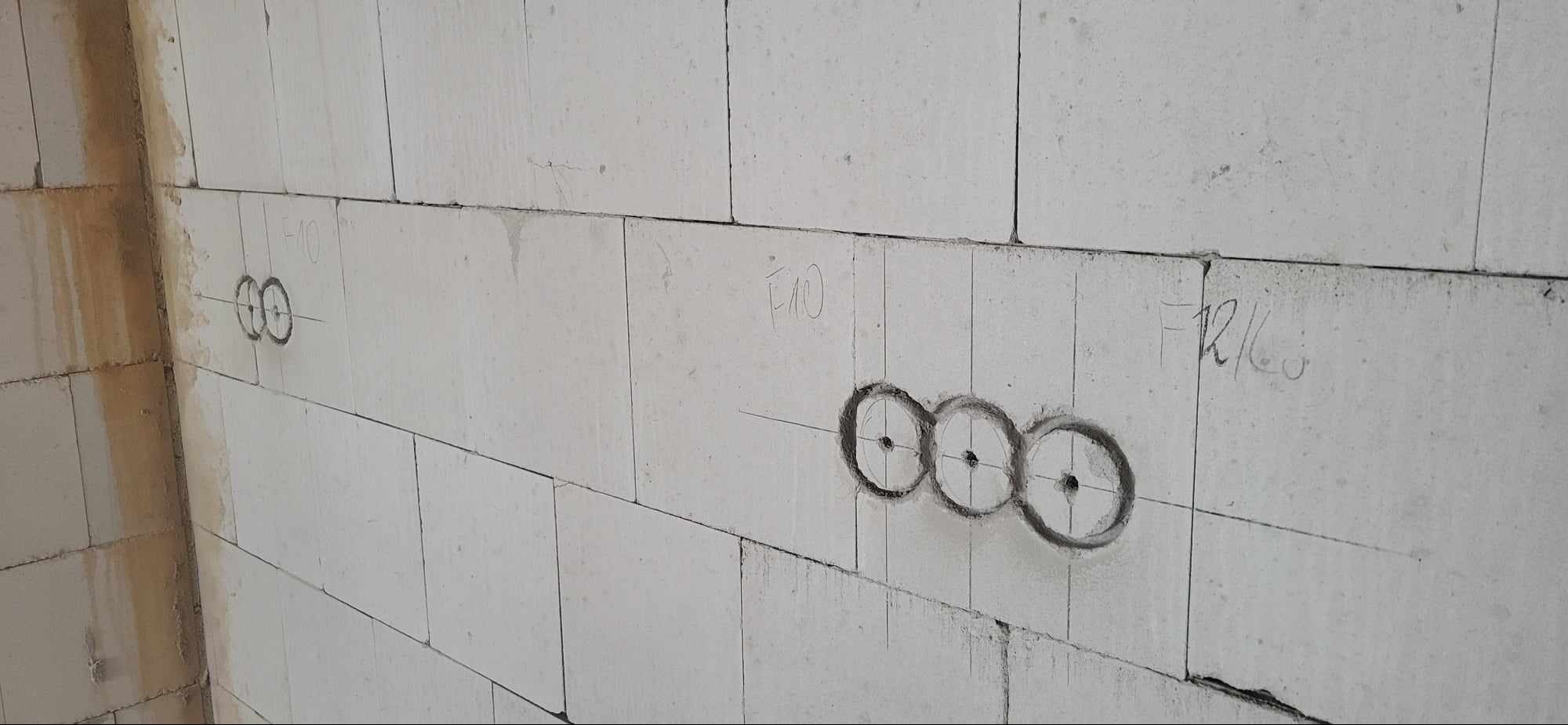 Ściana z betonu komórkowego z zaznaczonymi otworami pod puszki elektryczne, widoczne linie pomocnicze i oznaczenia ołówkiem.