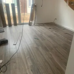 Układanie podłogi z paneli imitujących drewno w nowym domu, widoczne niedokończone schody, okno i przygotowane panele.