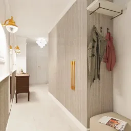 Wnętrze przedpokoju w jasnych barwach z elementami złota: lampy, uchwyty, wieszaki. Na ścianie tapeta w pionowe paski, a na pufie leży gazeta.