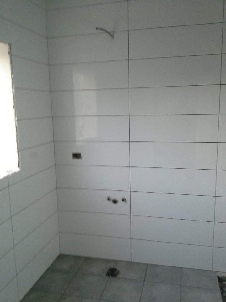 Wnętrze łazienki w trakcie wykańczania, widoczne białe, prostokątne płytki ścienne z ciemną fugą, szare płytki podłogowe i przygotowane otwory na armaturę.