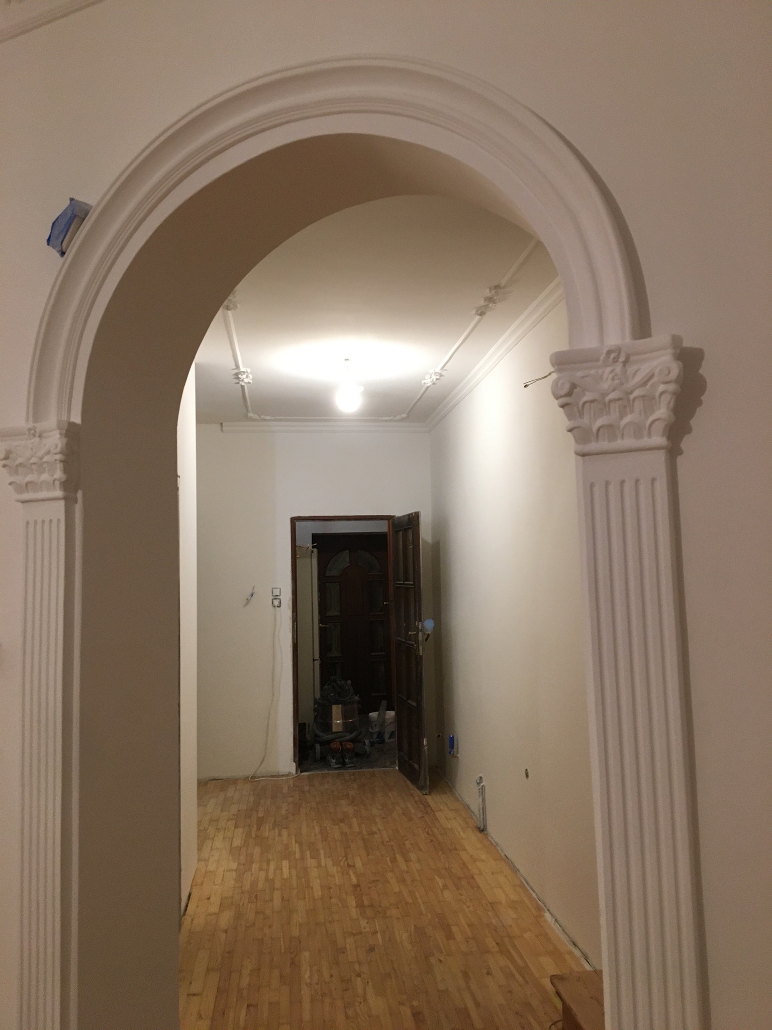 Wnętrze mieszkania z wykończonym łukiem z kolumnami, widok na parkiet i otwarte drzwi do kolejnego pomieszczenia, na ścianach widoczne ślady po pracach wykończeniowych.