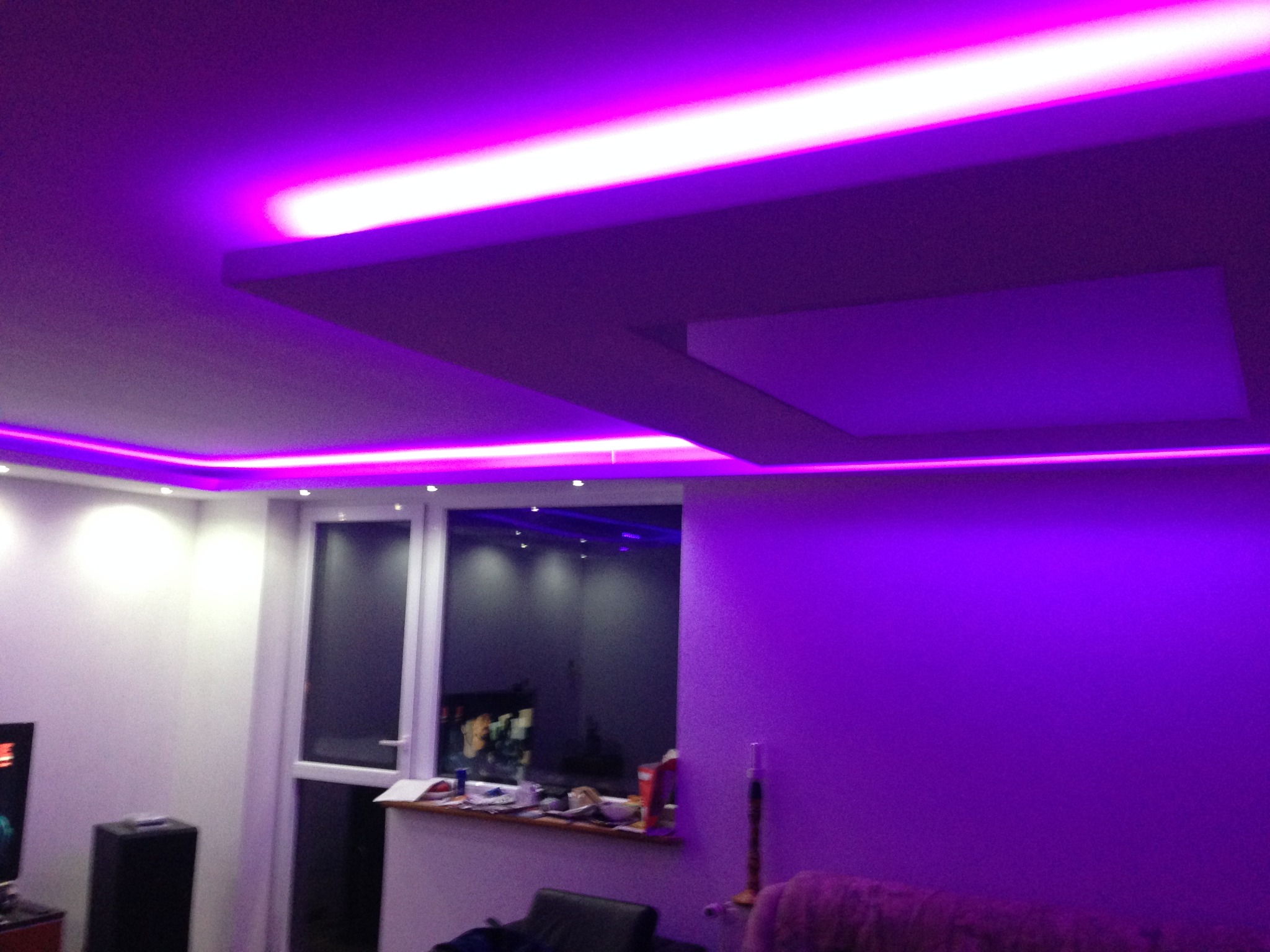 Nowoczesne oświetlenie sufitowe LED w odcieniach fioletu, z widoczną konstrukcją podwieszanego sufitu i fragmentem okna balkonowego w tle.