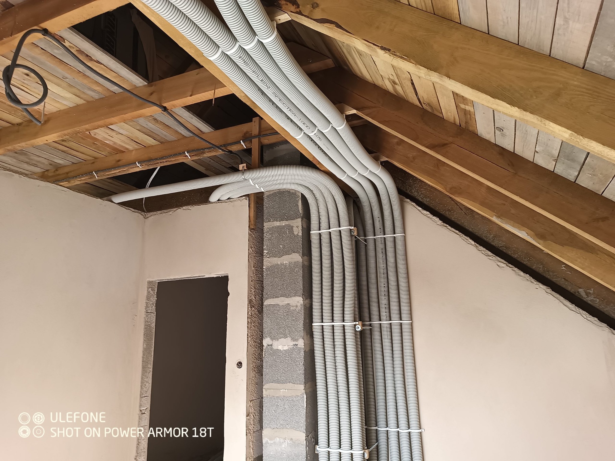 Montaż elastycznych rur wentylacyjnych w surowym wnętrzu poddasza, widoczne drewniane elementy konstrukcyjne dachu i ściany z betonu komórkowego.