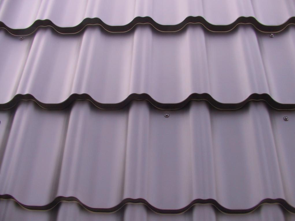 Szare, metalowe pokrycie dachowe typu blachodachówka, mocowane za pomocą wkrętów, z widocznymi falami i zaokrąglonymi krawędziami.