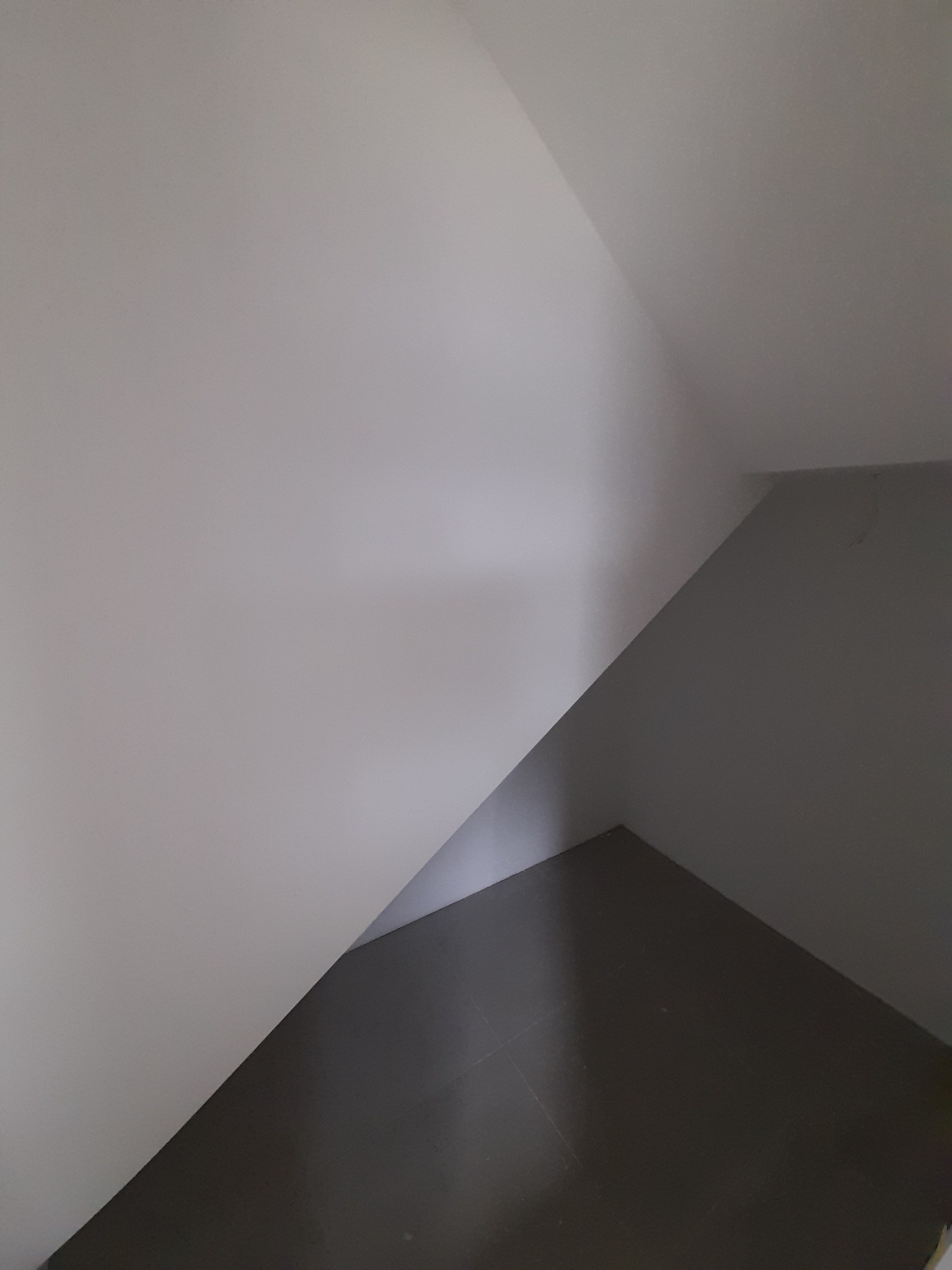 Świeżo pomalowane, białe ściany pod skosem i ciemna podłoga w rogu pokoju.