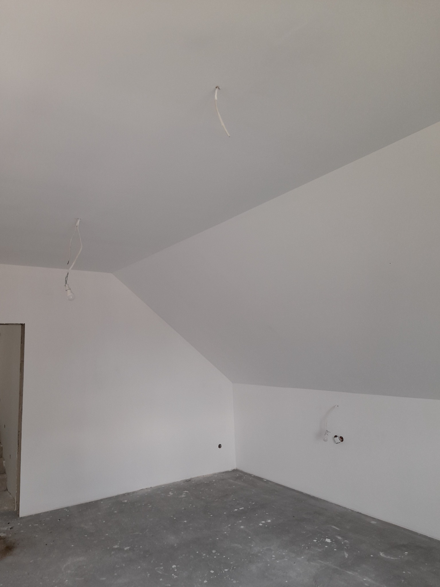 Wnętrze poddasza po malowaniu ścian na biało, widoczne przygotowane punkty elektryczne i surowa betonowa podłoga.