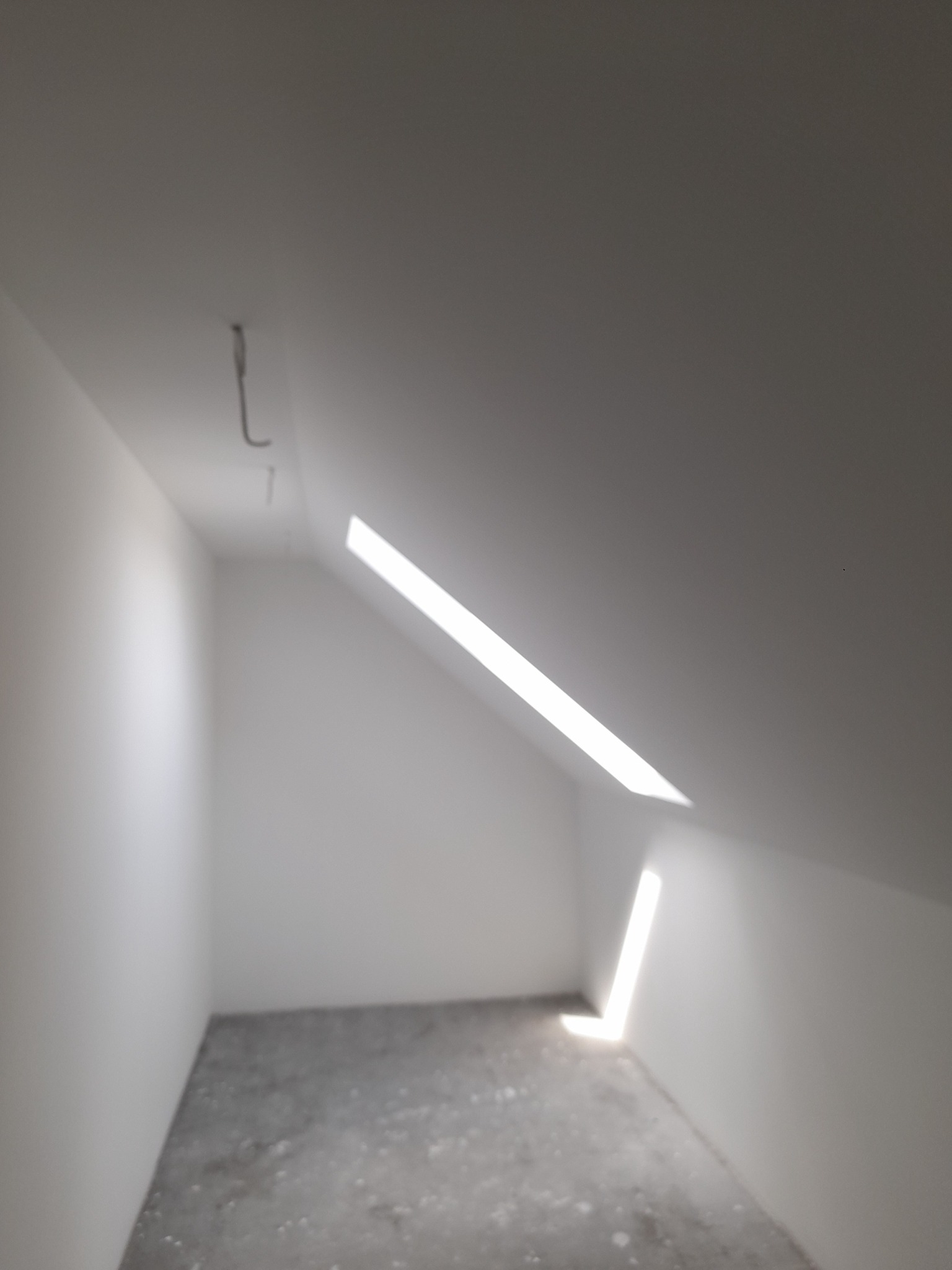 Poddasze ze świeżo pomalowanymi białymi ścianami, widoczny fragment okna dachowego wpuszczającego smugi światła.