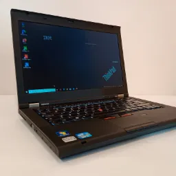 Czarny laptop Lenovo ThinkPad T430 z podświetlaną klawiaturą, widoczny ekran z ikonami programów i logo IBM, naklejki Windows 7 i Intel Core i5 na obudowie, ustawiony na białym tle.
