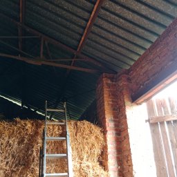 BW-Computers Bogusz Wawrzyniak - Wnętrze stodoły z belami siana, oparta o nie aluminiowa drabina, widoczna ceglana ściana i metalowy dach.