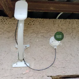 Zewnętrzna kamera monitoringu z anteną zamontowana na szarej, chropowatej ścianie pod zadaszeniem z widocznymi elementami konstrukcji stalowej.