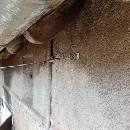 BW-Computers Bogusz Wawrzyniak - Zewnętrzna instalacja kabla odgromowego przymocowanego do ściany budynku z widoczną rynną i drewnianym elementem konstrukcyjnym dachu.