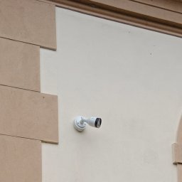 BW-Computers Bogusz Wawrzyniak - Biała kamera monitoringu zamontowana na kremowej elewacji budynku z dekoracyjnymi elementami architektonicznymi w kolorze piaskowym.