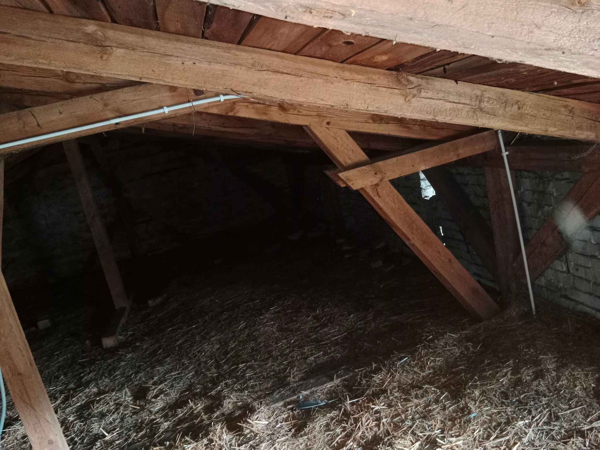 Strych z drewnianą konstrukcją dachu, izolacją z siana i instalacją elektryczną w białej rurce PCV.