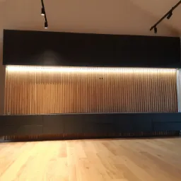 Grafitowa zabudowa RTV z lamelami dębowymi, podświetlana listwą LED, widoczna na tle parkietu i zasłony.