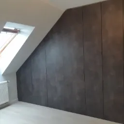 Szafa wnękowa z ciemnoszarymi frontami dopasowana do skosu dachu, widoczny grzejnik i okno dachowe.