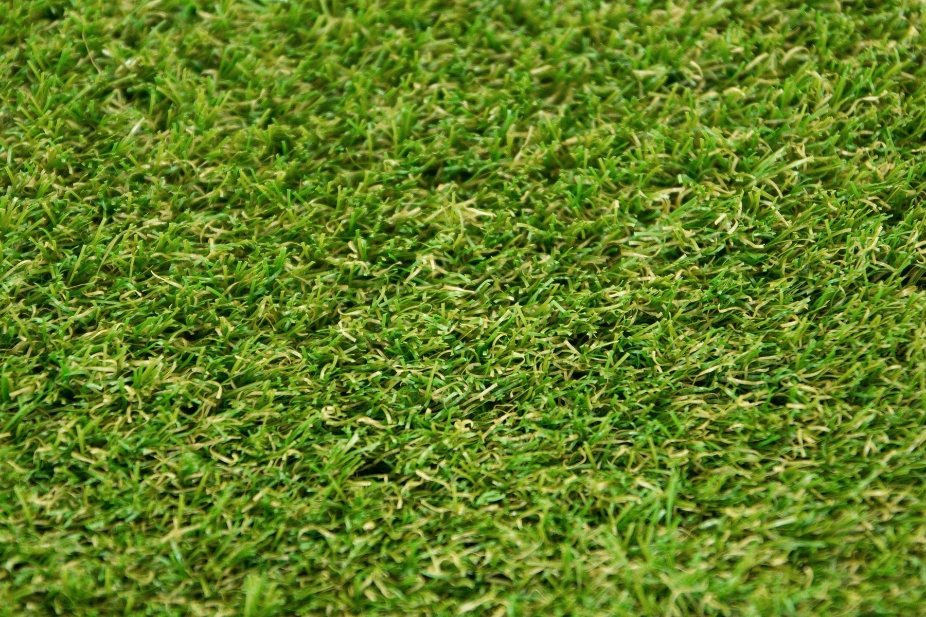 Bliski kadr na zieloną, syntetyczną trawę z rolki, ukazujący strukturę włókien i ich odcienie.