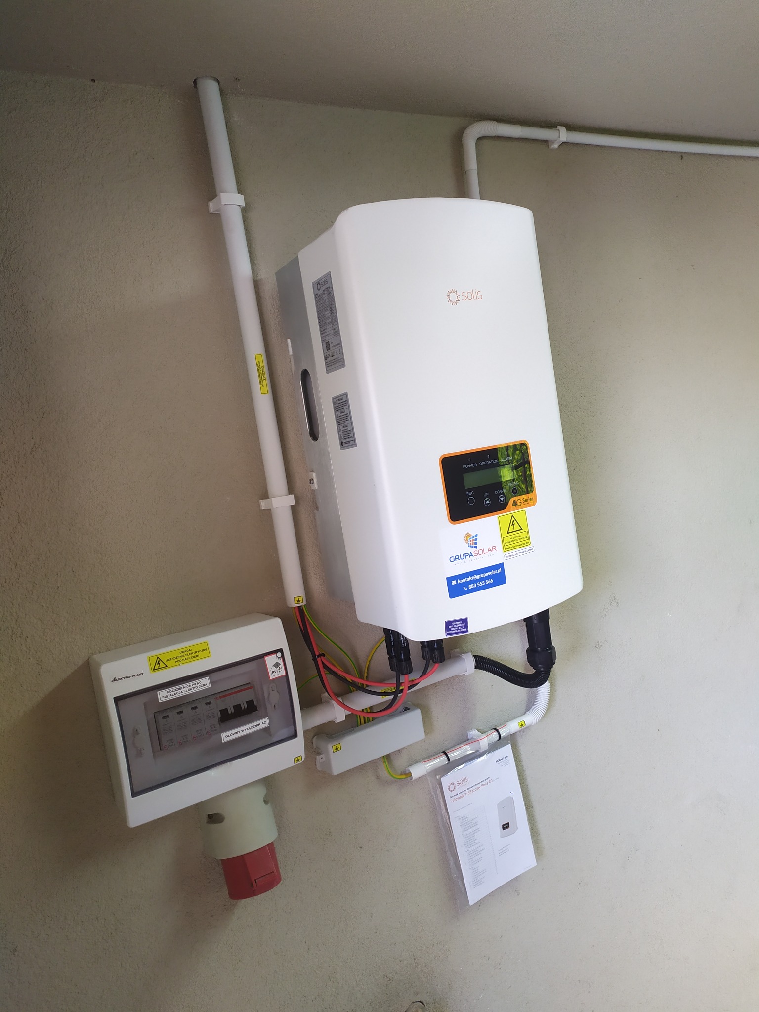 Zamontowany falownik Solis 4G na ścianie, obok skrzynka rozdzielcza Elektro-Plast i rury instalacyjne, widoczna dokumentacja falownika.