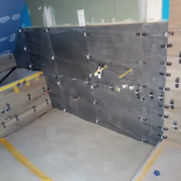 Ściana łazienki w trakcie układania płytek: ciemnoszare płytki imitujące kamień sąsiadują z jasnymi, drewnopodobnymi, widoczne krzyżyki dystansowe, przygotowane otwory na instalację wodną...