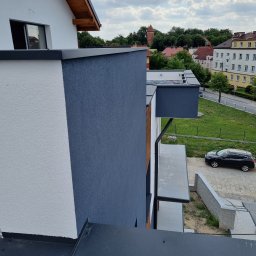 Małryl Z.P.U Przemysław Lewna - Nowoczesna elewacja budynku z wyraźnym podziałem na białą i grafitową część, widok z góry, w tle zabudowa miejska i błękitne niebo z chmurami.