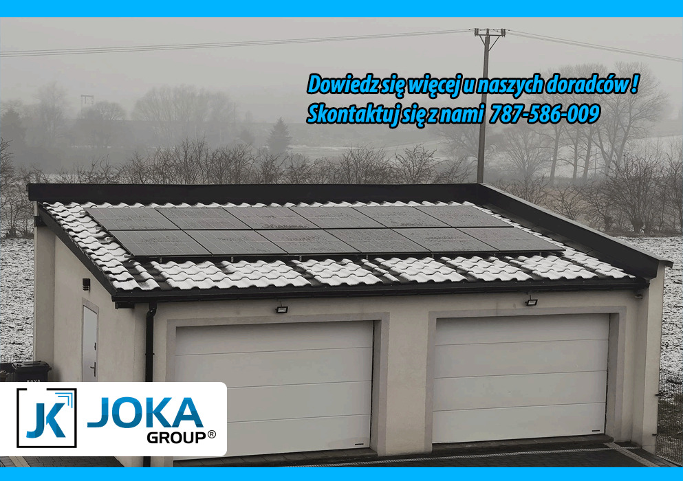 Panele fotowoltaiczne na dachu garażu dwustanowiskowego pokrytego śniegiem, logo firmy JOKA GROUP w lewym dolnym rogu, zima w tle.