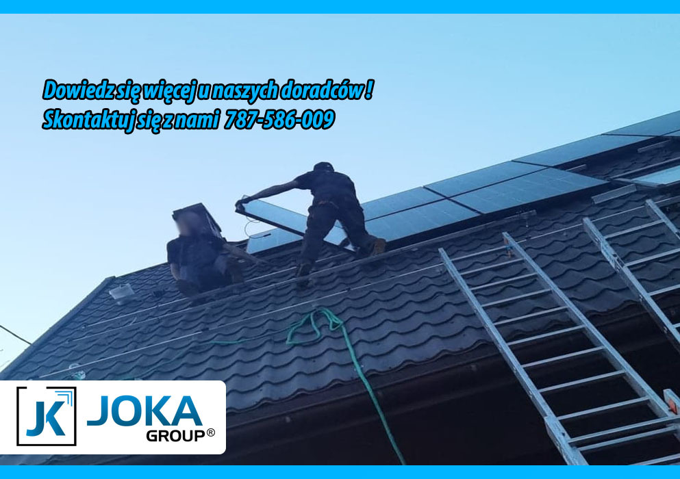 Montaż paneli słonecznych na dachu z metalową dachówką, widoczne dwie osoby przy pracy, drabina oparta o dach, w tle błękitne niebo oraz logo firmy JOKA Group z hasłem reklamowym.