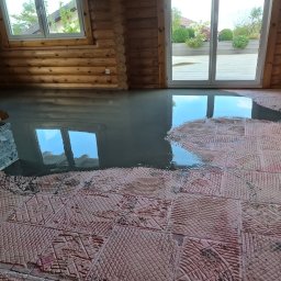 Ecobat Sarl - Wylewka samopoziomująca na podkładzie z płytek w drewnianym domu z widocznym kominkiem i oknem.