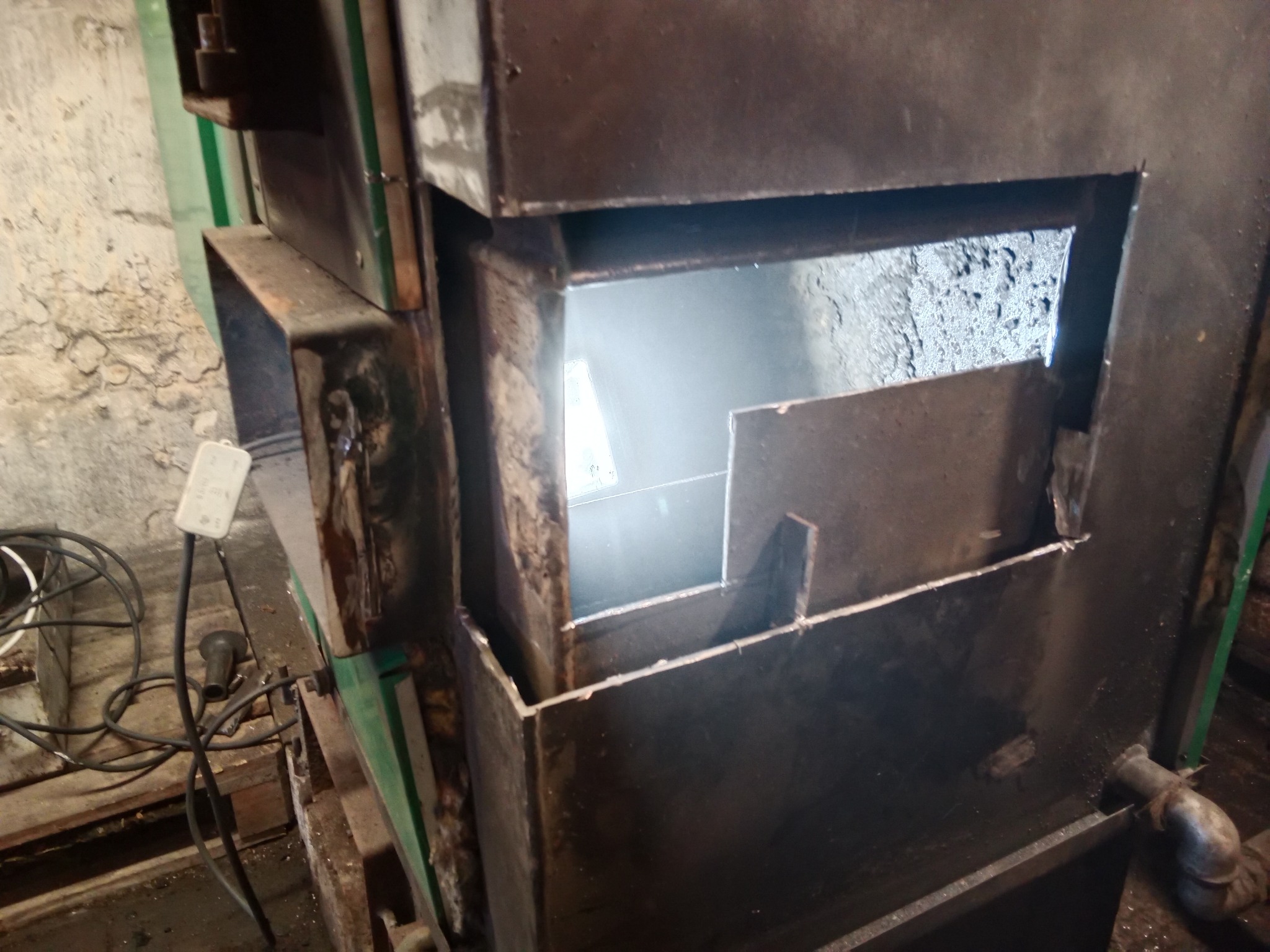 Wnętrze metalowej konstrukcji, prawdopodobnie pieca lub kotła, z widocznymi spawami i elementami montażowymi, otoczone surowymi ścianami i przewodami elektrycznymi.