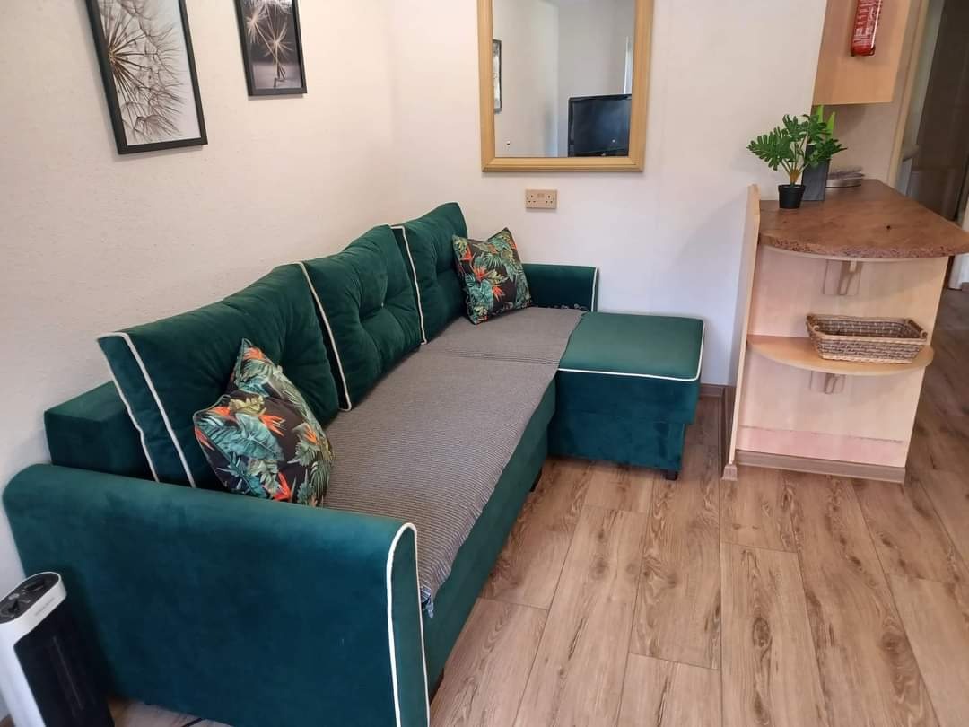 Salon z zieloną sofą narożną z białym obszyciem, drewnianą podłogą i dekoracjami ściennymi w postaci czarno-białych grafik.