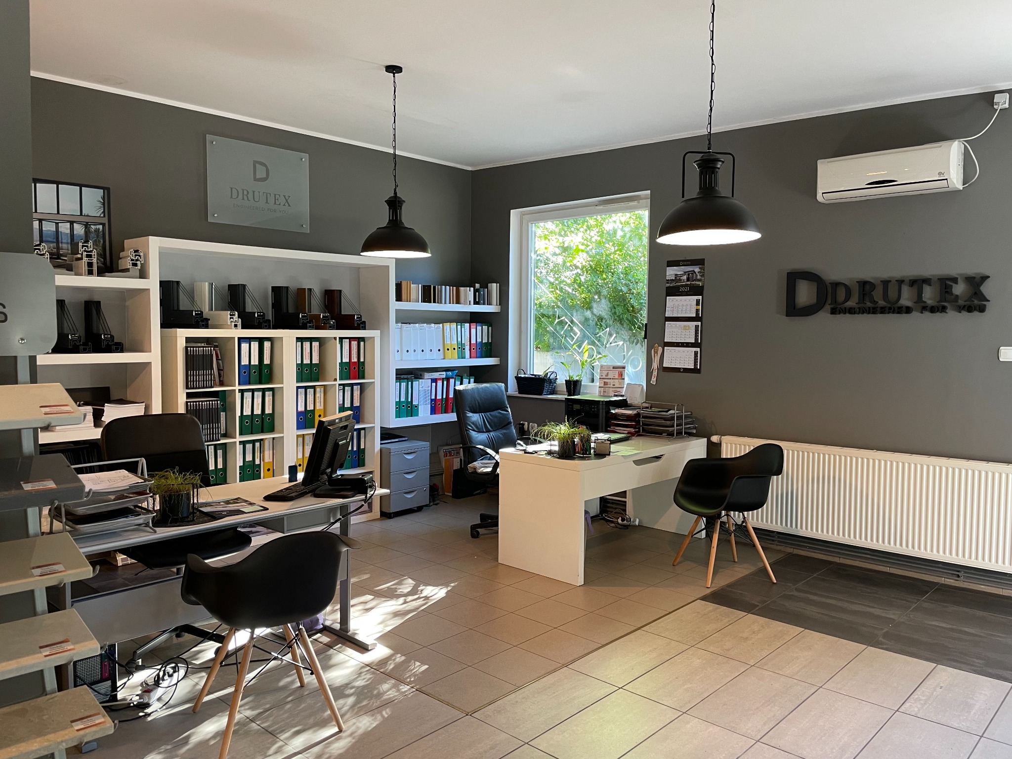 Wnętrze biura firmy Drutex z ekspozycją profili okiennych, biurkami, krzesłami i logo firmy na ścianie.