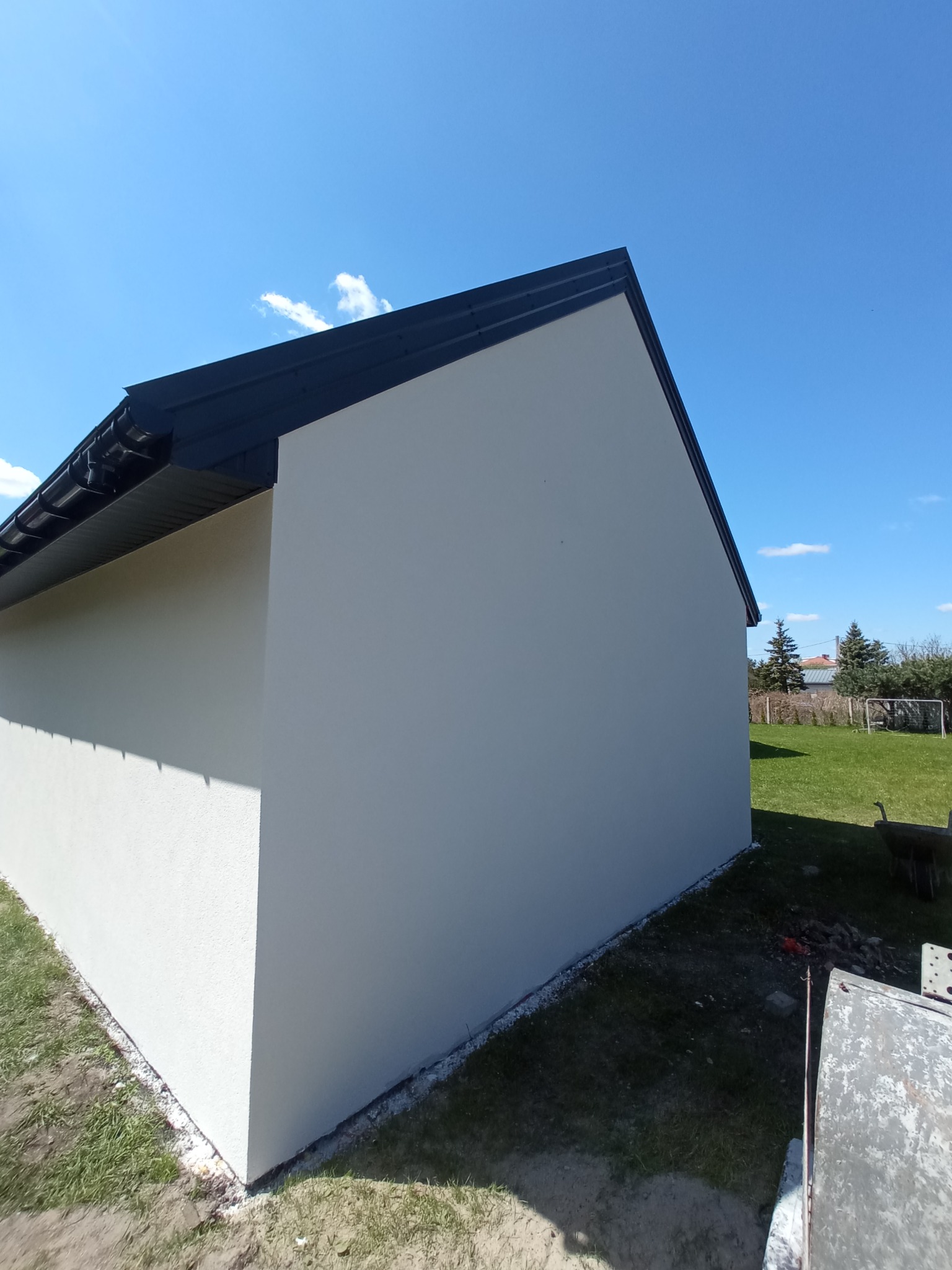 Ściana budynku z nowym, ciemnym orynnowaniem i jasnym tynkiem, widok z zewnątrz w słoneczny dzień.