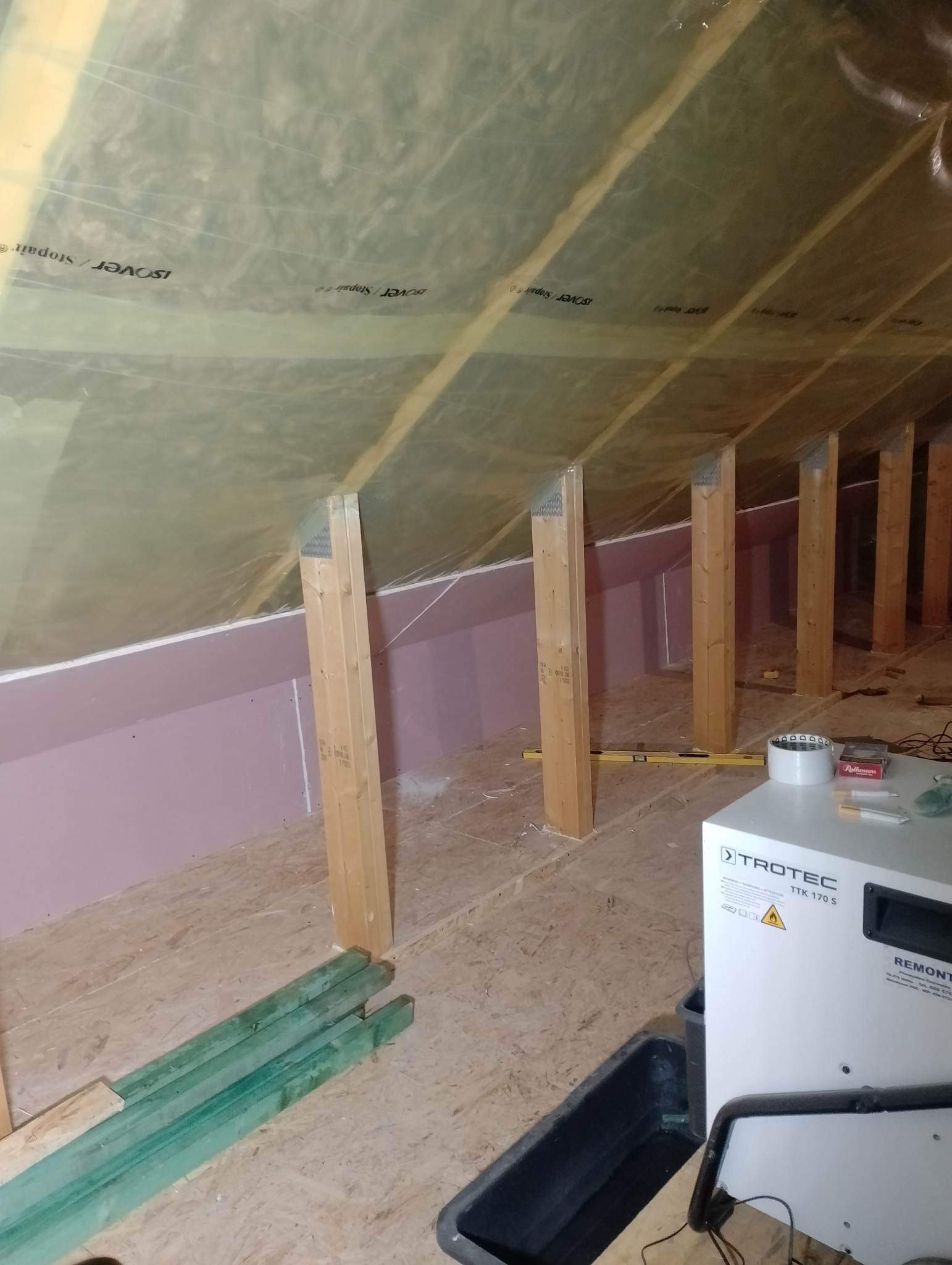 Poddasze w trakcie ocieplania, widoczne drewniane słupki, wełna mineralna Isover Stopair pod folią, płyty karton-gips na ścianach, poziomica, oraz osuszacz powietrza Trotec TTK 170 S.