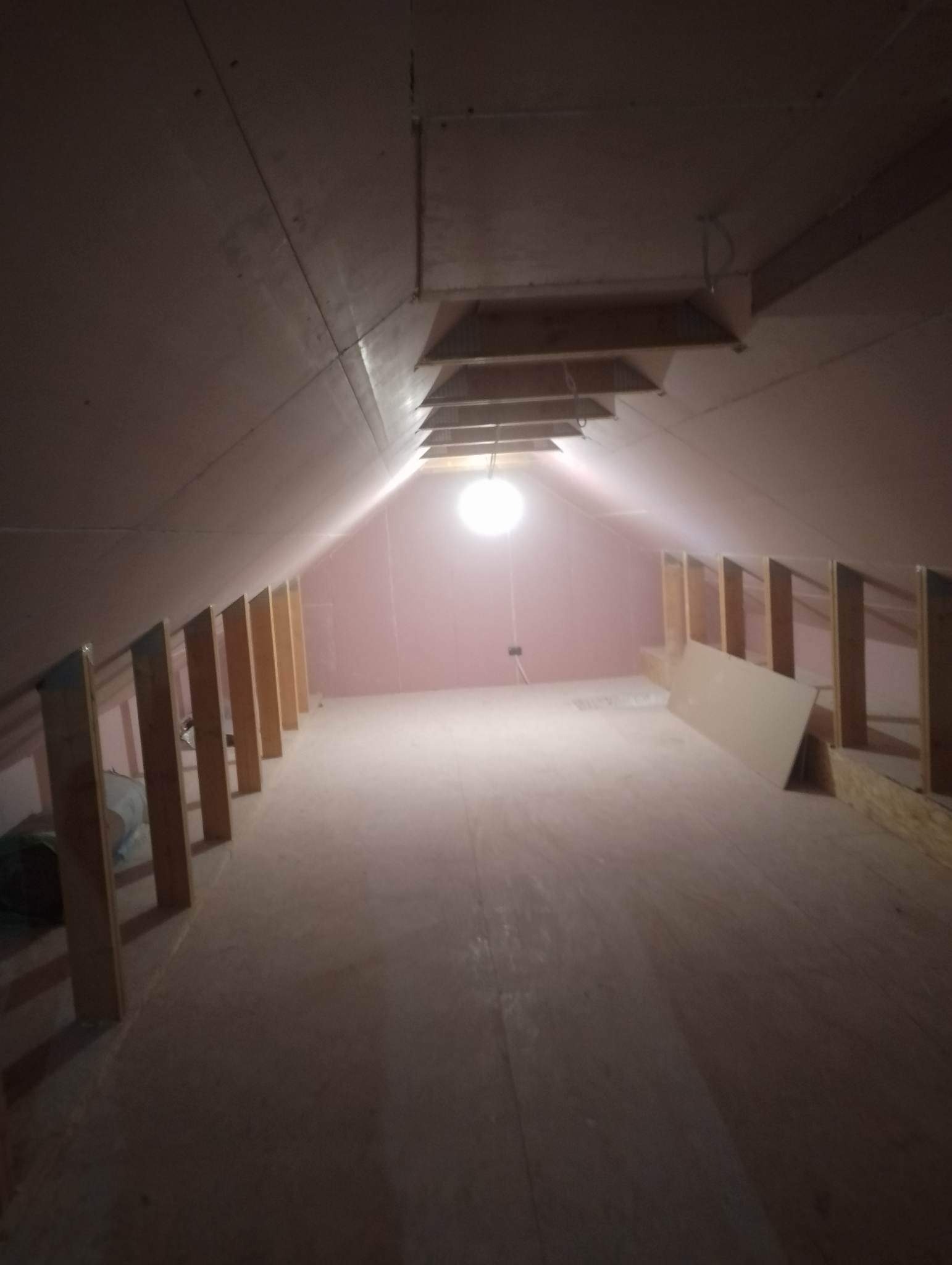 Poddasze w trakcie adaptacji z widocznymi elementami konstrukcyjnymi ścianek działowych i ocieplenia poddasza wełną mineralną, sufit wykończony płytami gipsowo-kartonowymi.