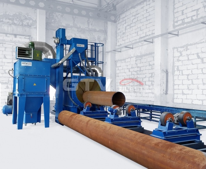 Automatyczna piaskarka przelotowa do rur stalowych z systemem transportu poprzecznego, widoczne elementy konstrukcyjne i rura w trakcie obróbki.